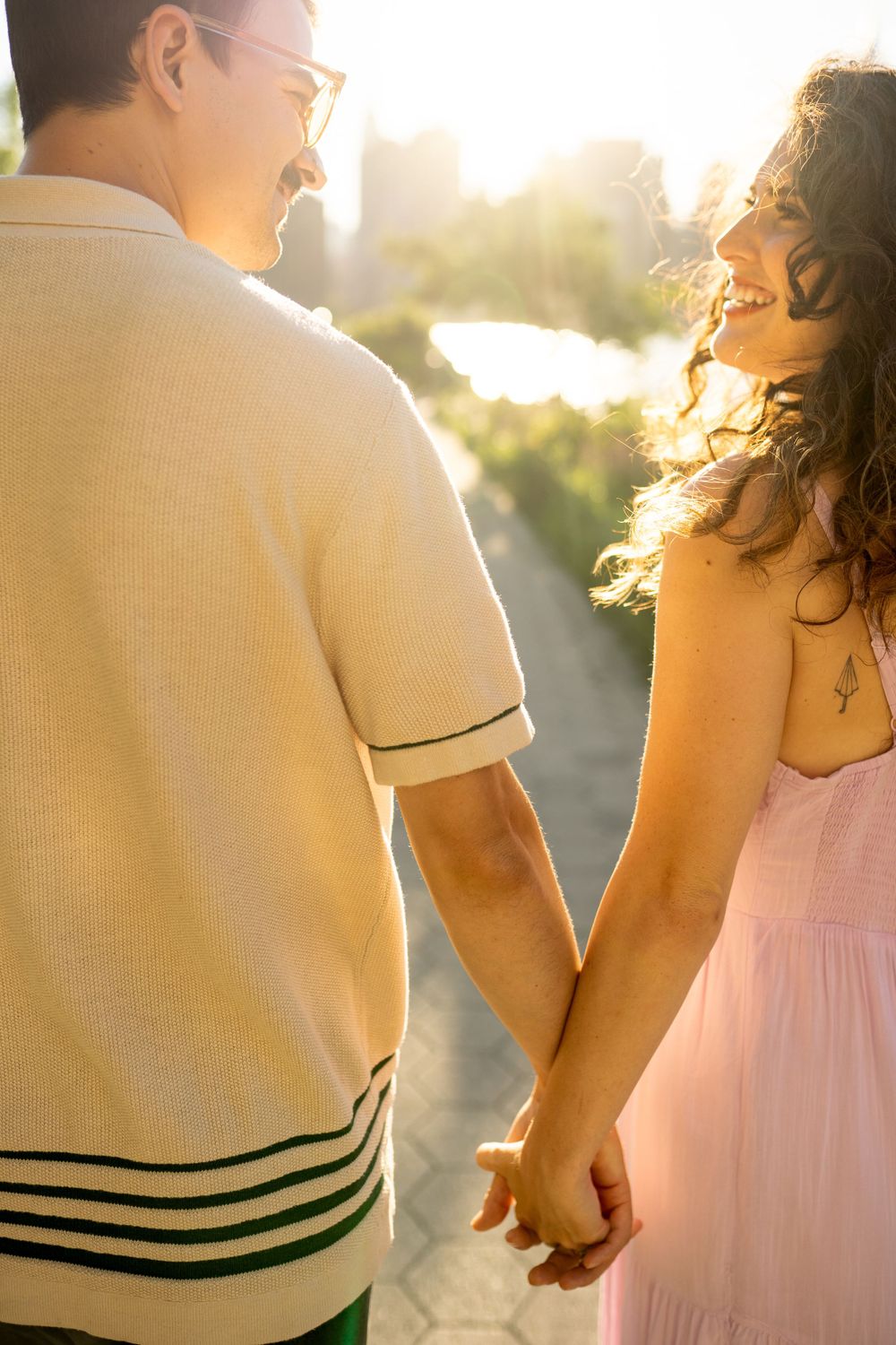 Two people in light-colored clothing hold hands against golden sunlight.