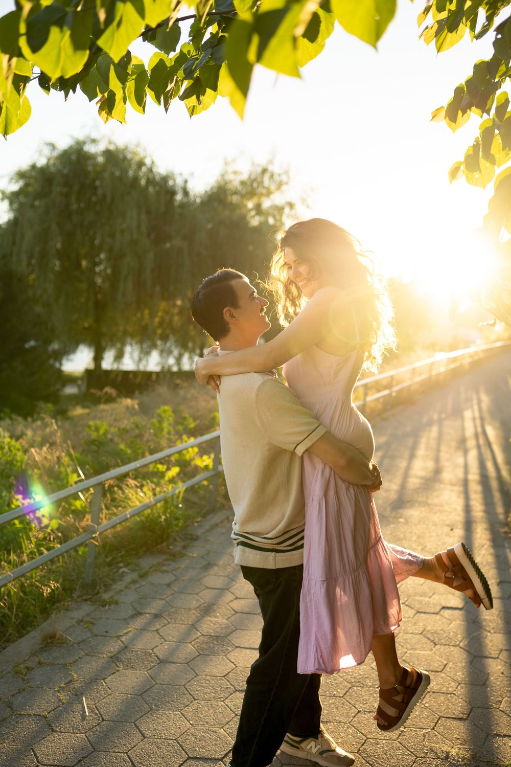A couple dances playfully on a path during golden hour beneath overhanging tree branches.
