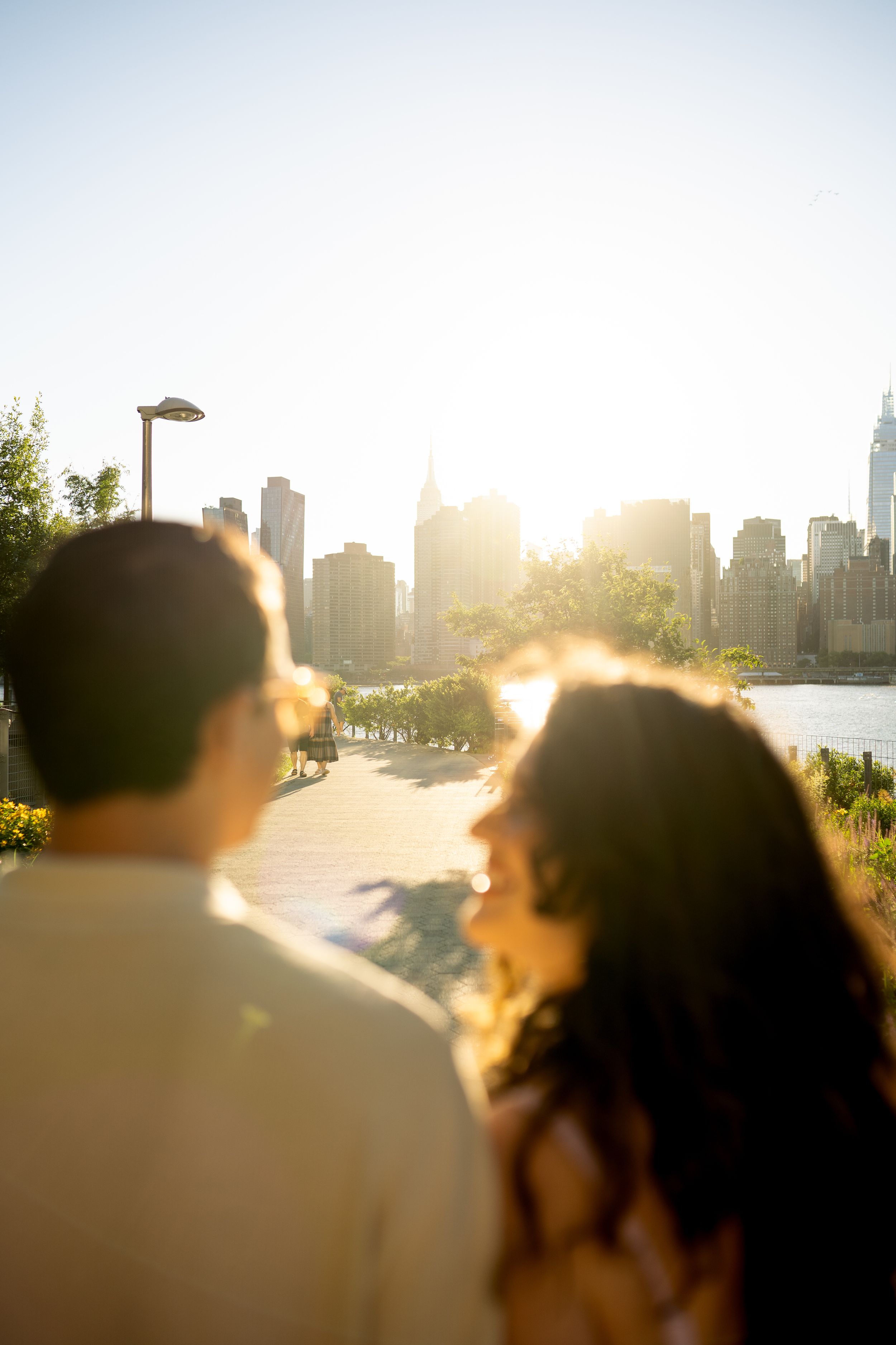 A couple gazes at a city skyline during sunset with buildings in the background.