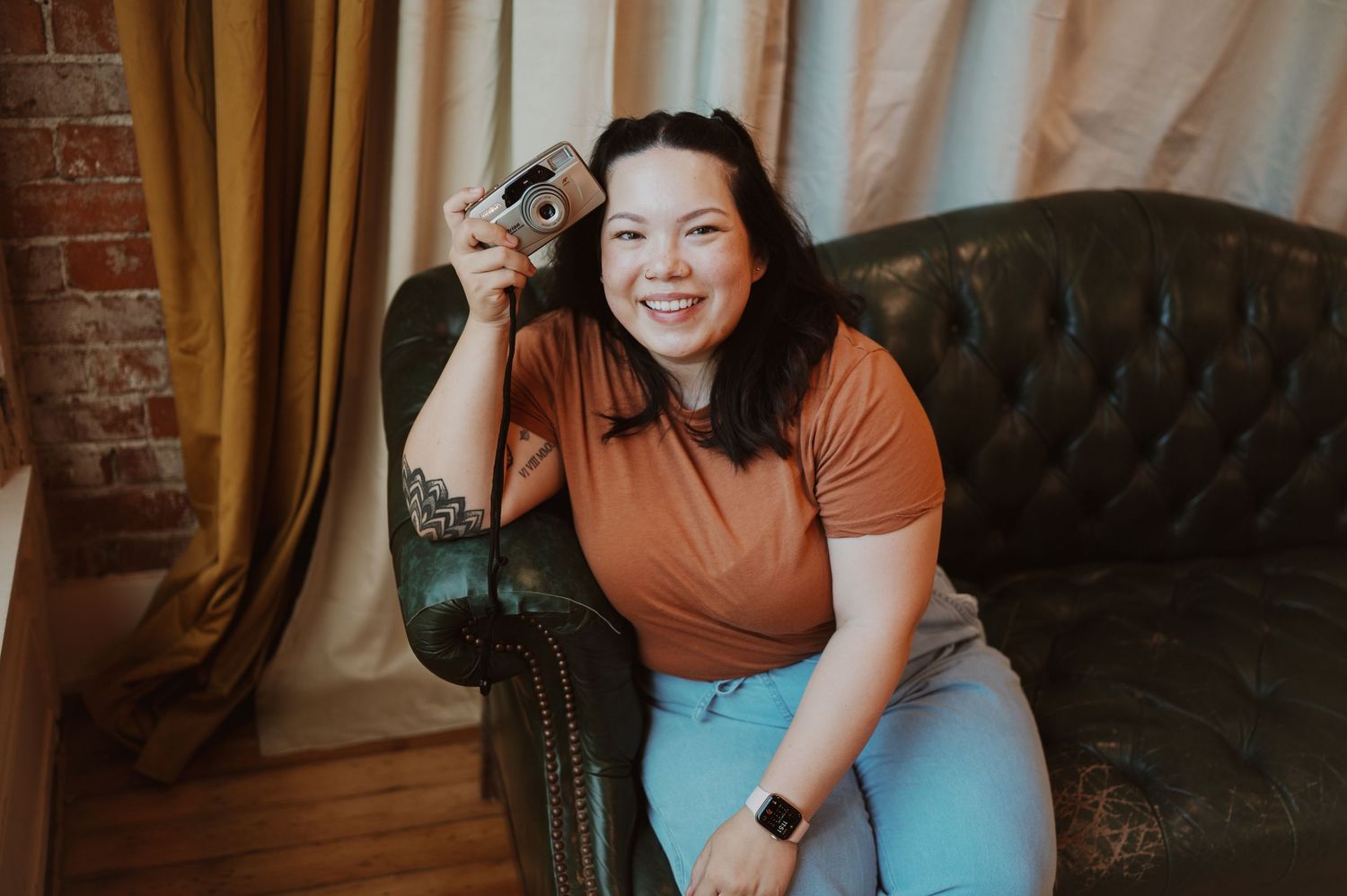 Person in casual attire sitting on vintage tufted couch against brick wall.