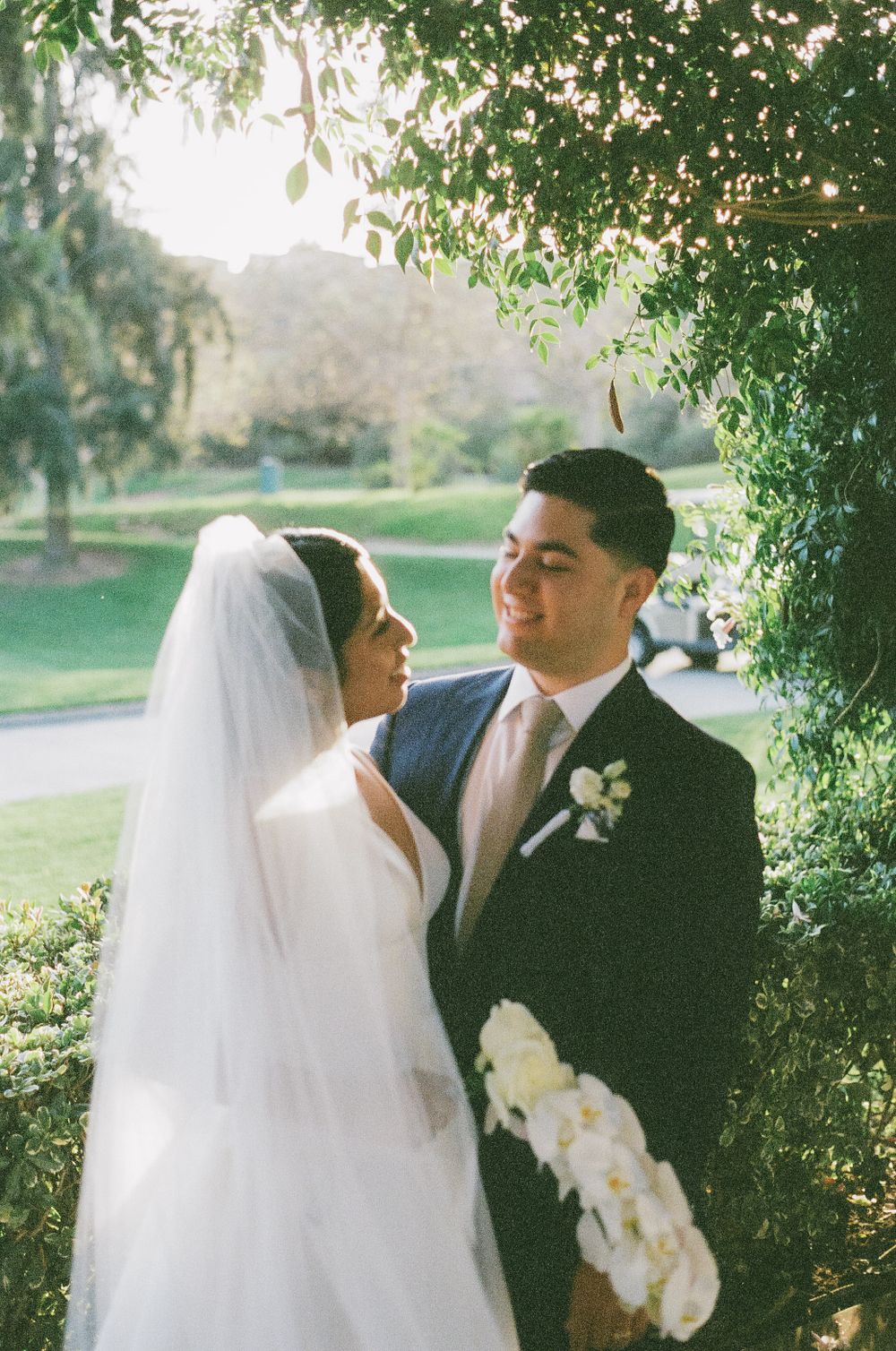 Intimate wedding moment captured under green foliage with white floral accents.