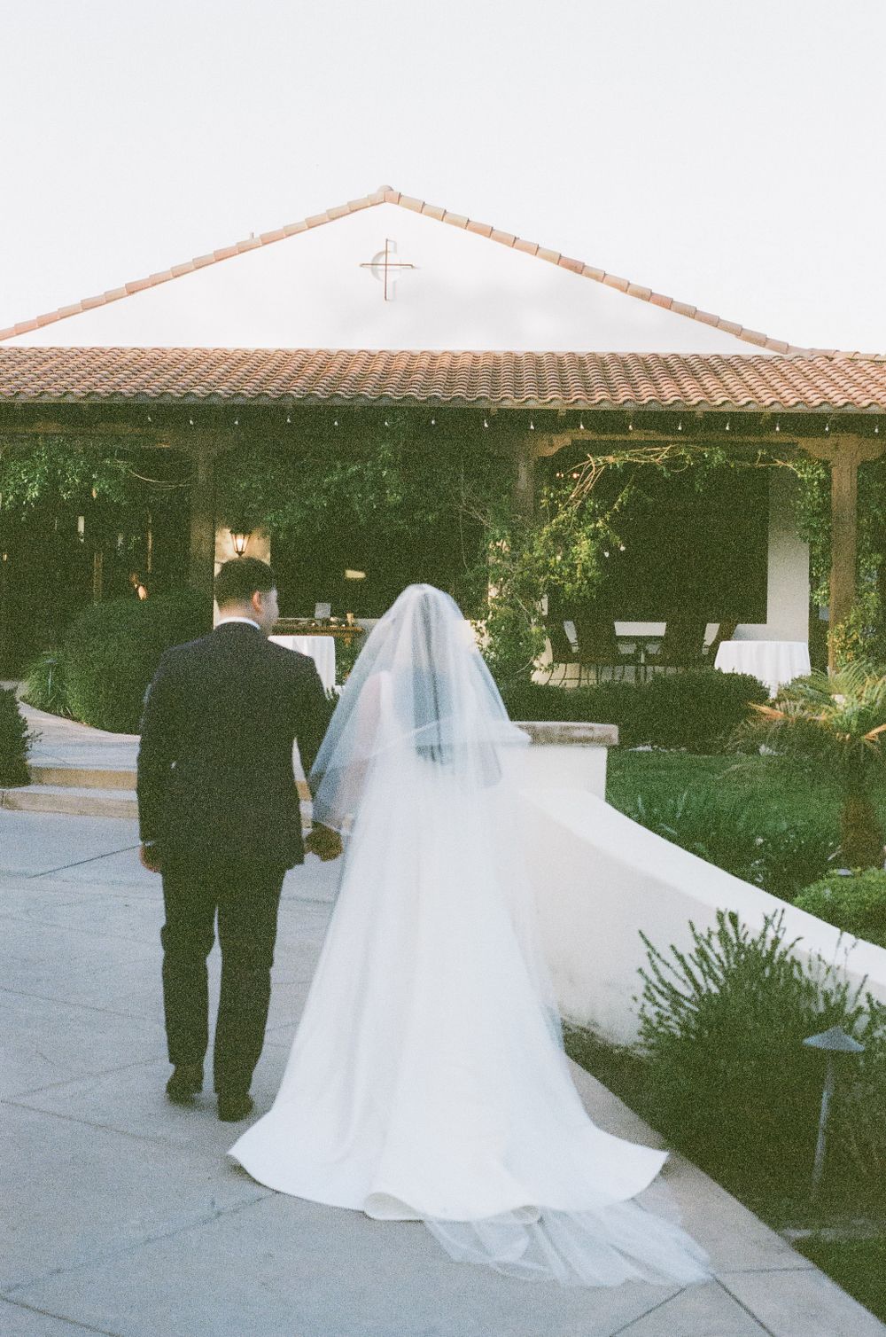Wedding couple walking along a Spanish-style courtyard with terra cotta roof.