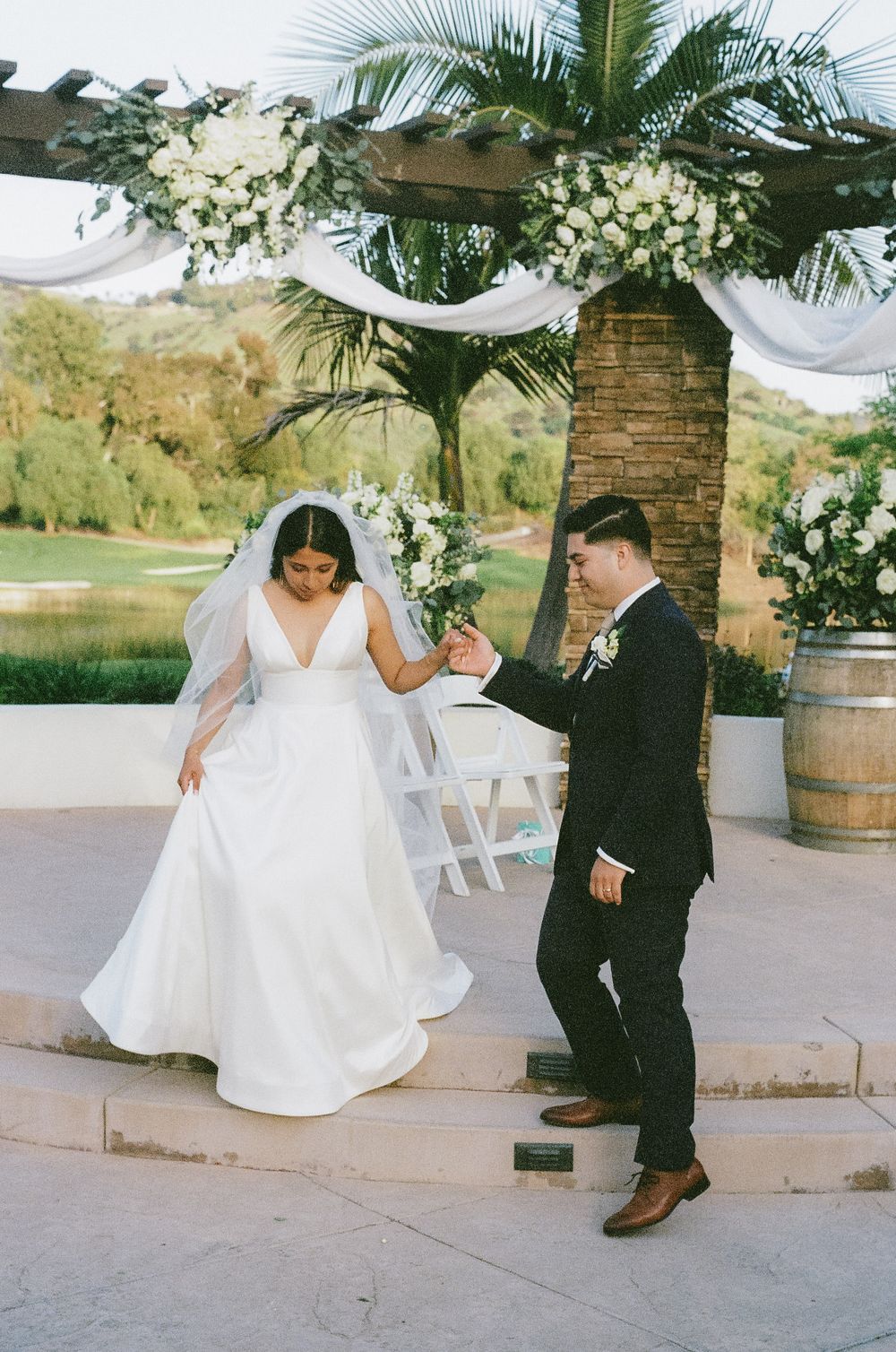 Wedding couple dances and twirls on a stone patio decorated with palm trees and white flowers.