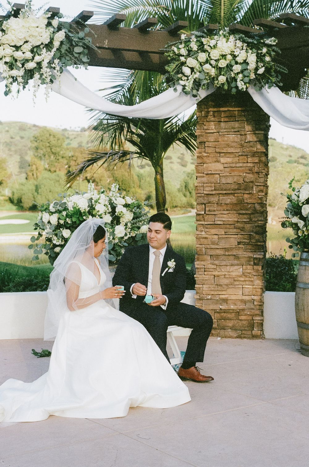 Bride and groom sit together on a decorated patio during their wedding celebration.