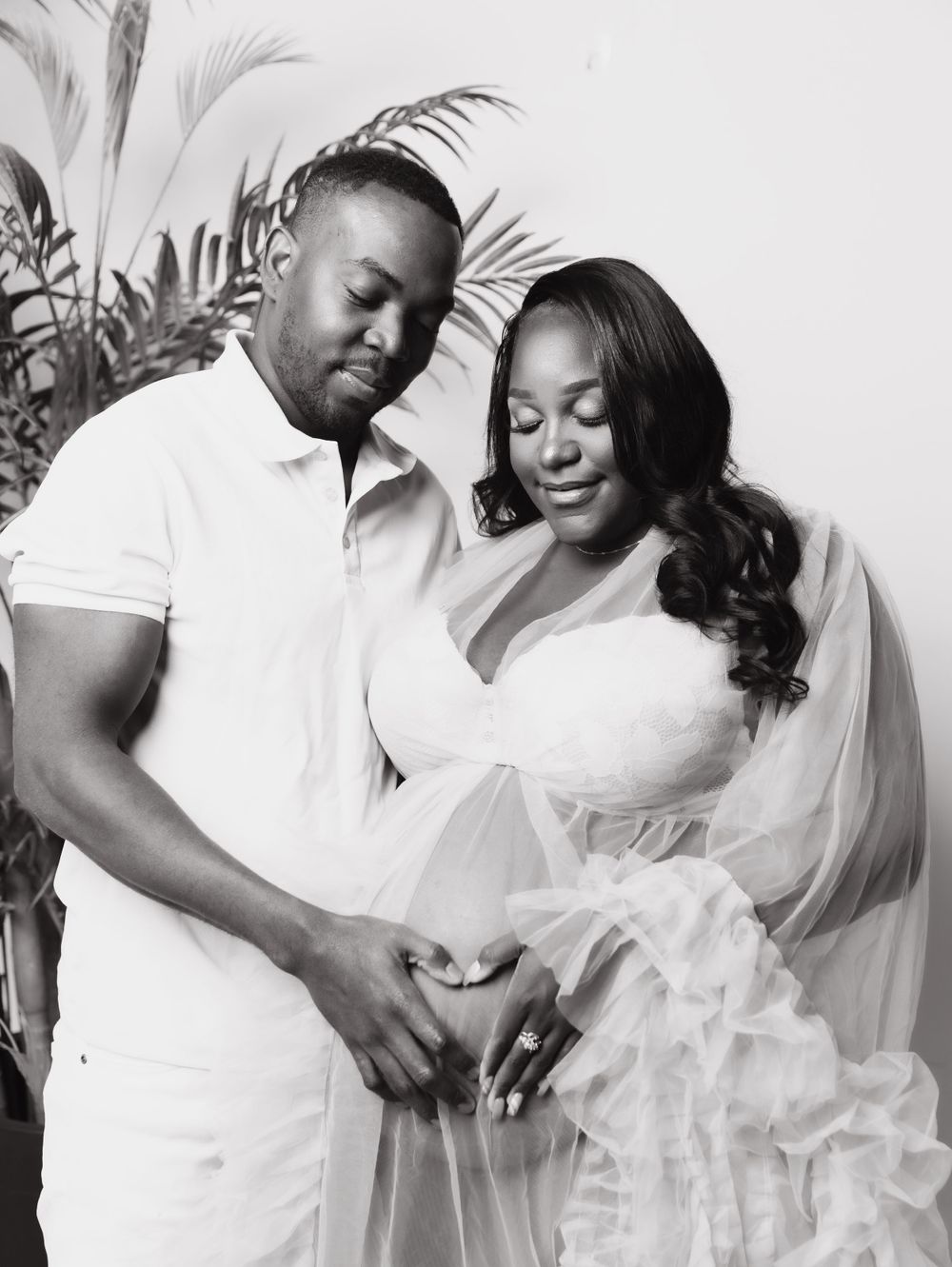 Couple in white outfits embrace for romantic maternity photo.