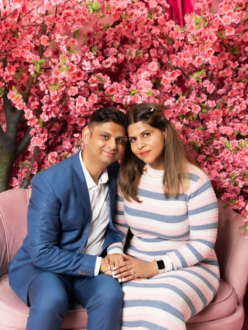 Couple sits on pink bench against backdrop of vibrant pink cherry blossoms.