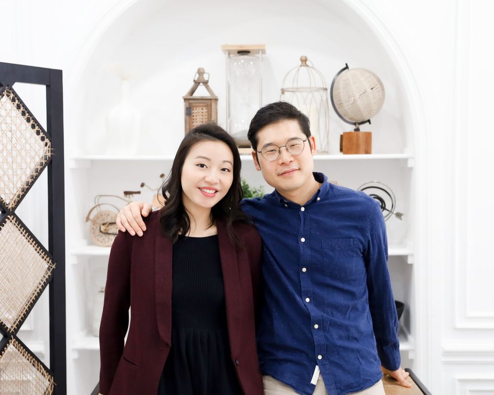 Couple in burgundy and navy casual attire posing in front of white built-in shelving.
