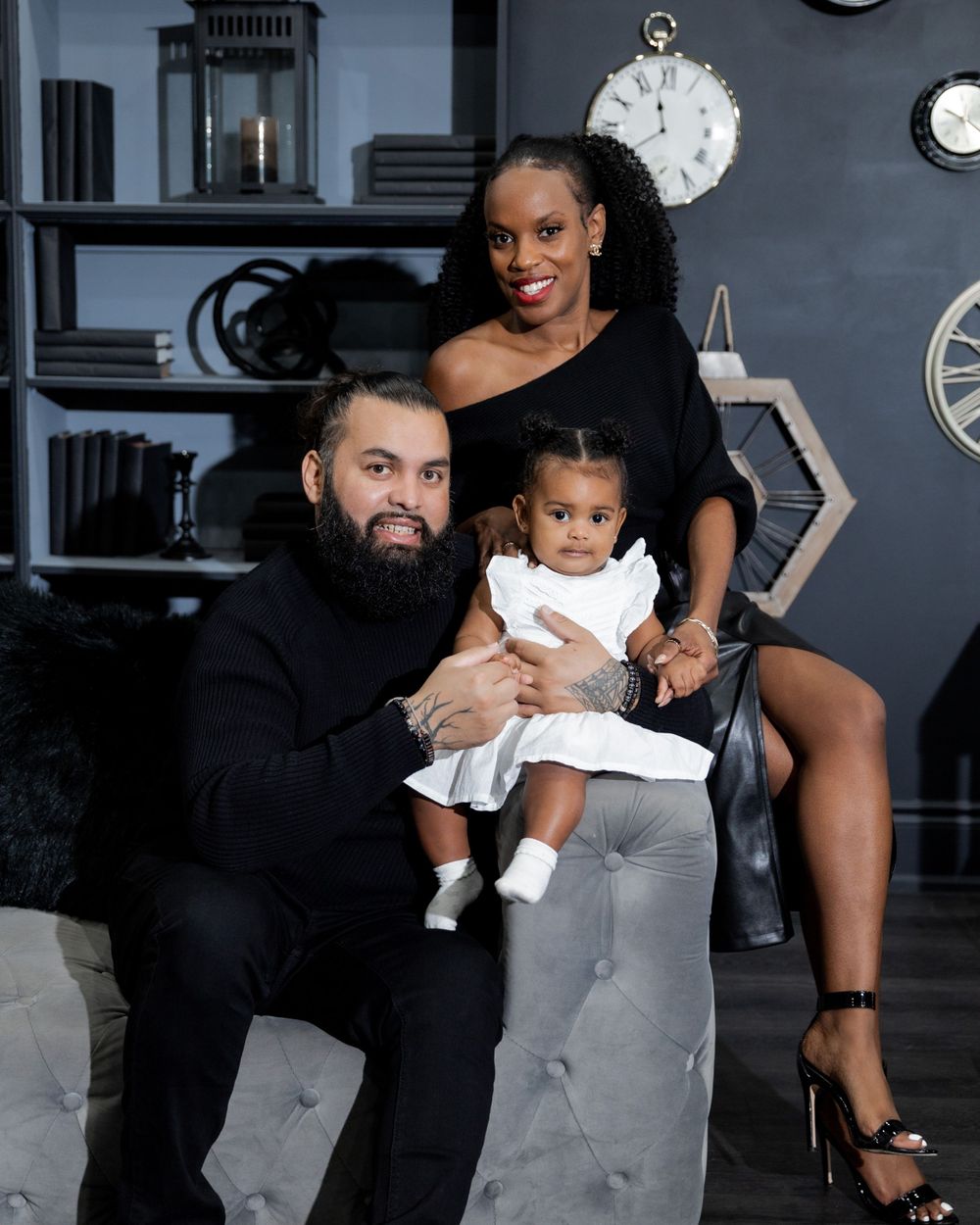 Studio family portrait with dark background and vintage clock decor elements.