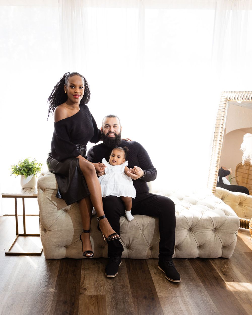 Family posed on tufted beige chaise in bright modern room setting.