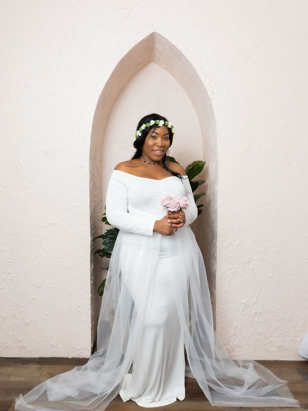 Woman in white wedding gown and floral crown poses in arched doorway.