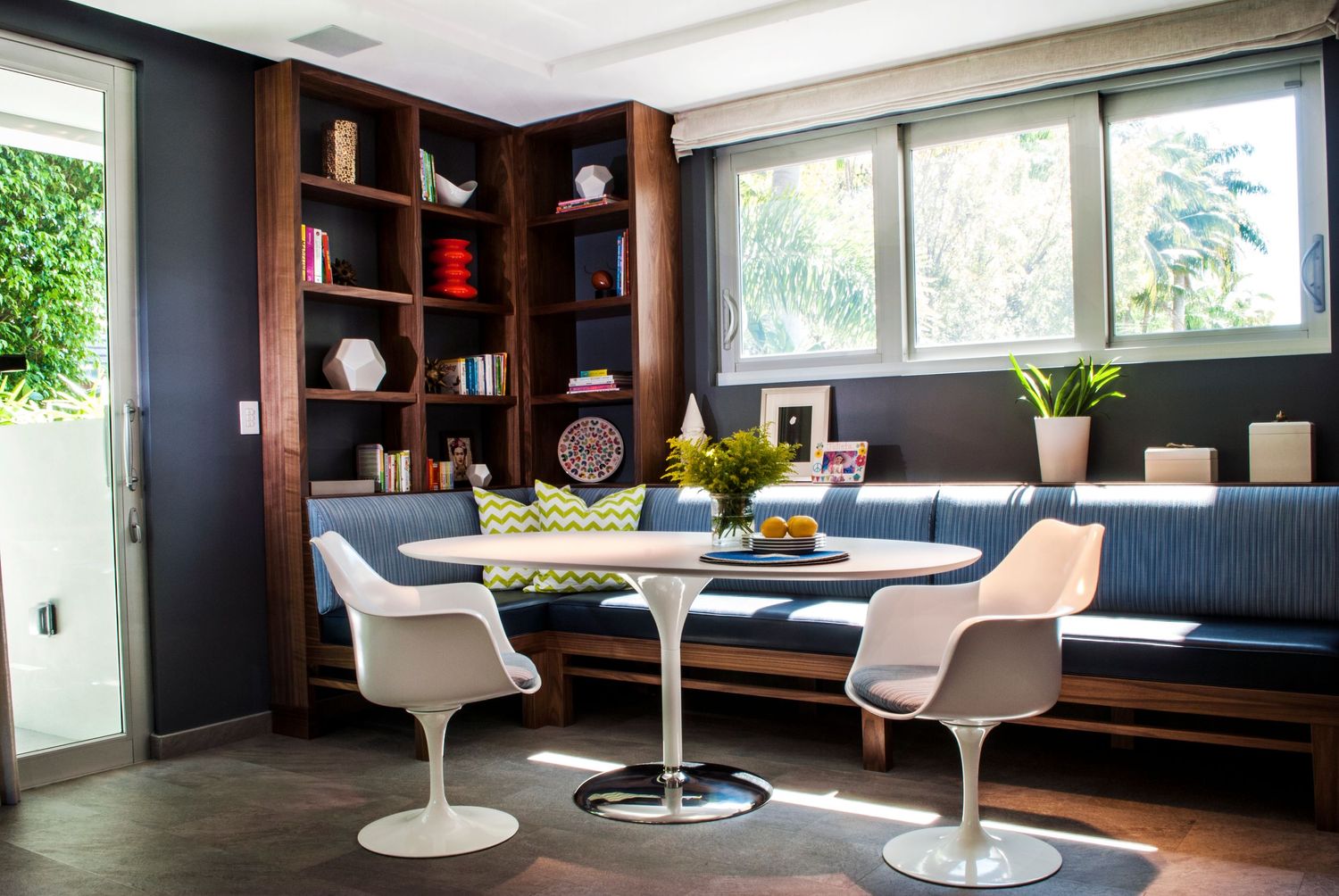 Modern dining nook with tulip chairs and built-in bench seating against navy blue walls.