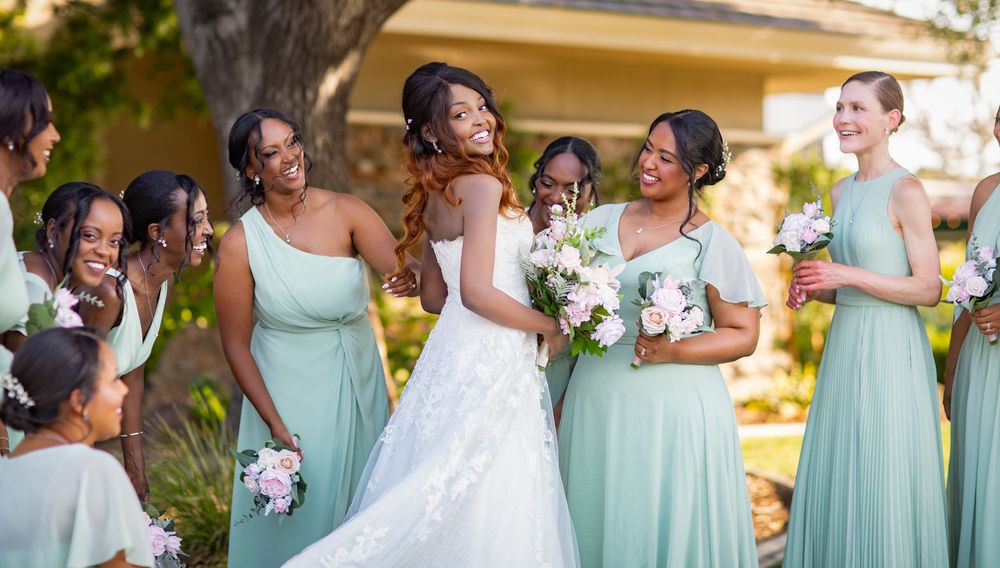 Wedding party wearing mint green bridesmaid dresses poses together in outdoor garden setting.
