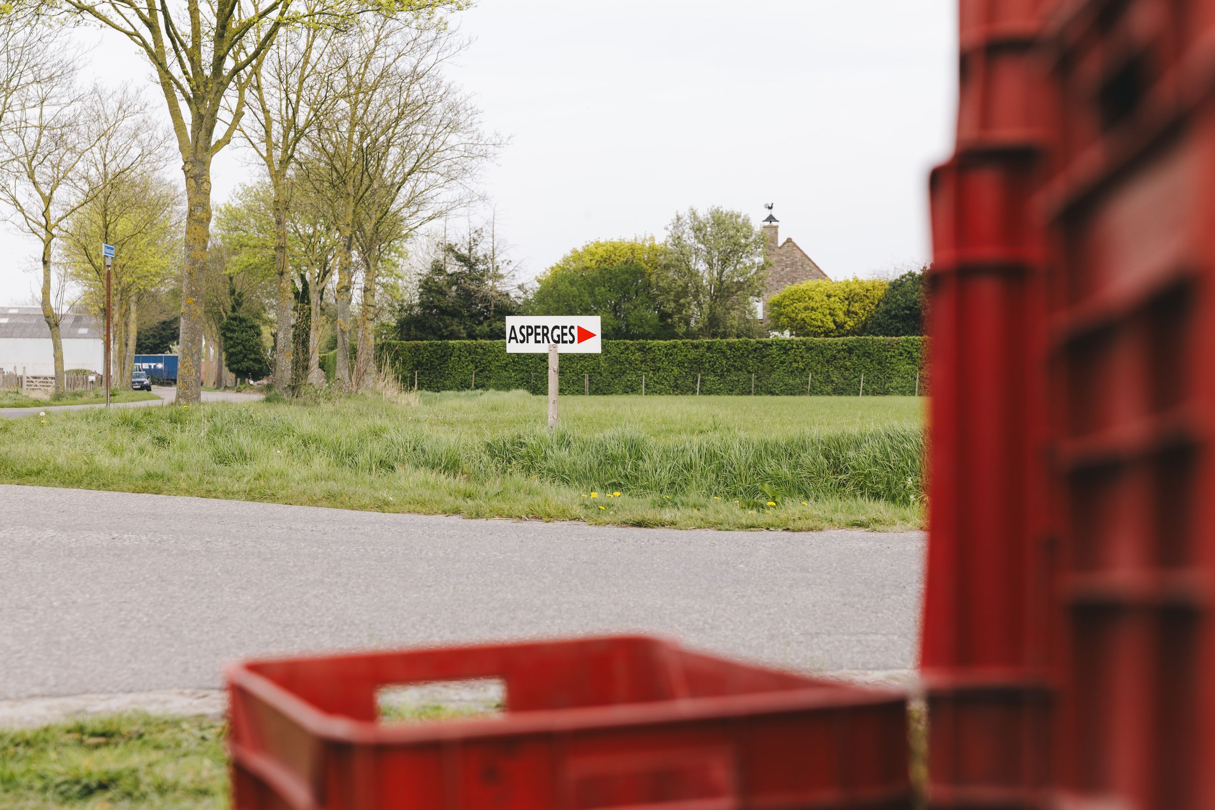 Red crates near a rural road with a directional sign and green trees beside a countryside house in the background.