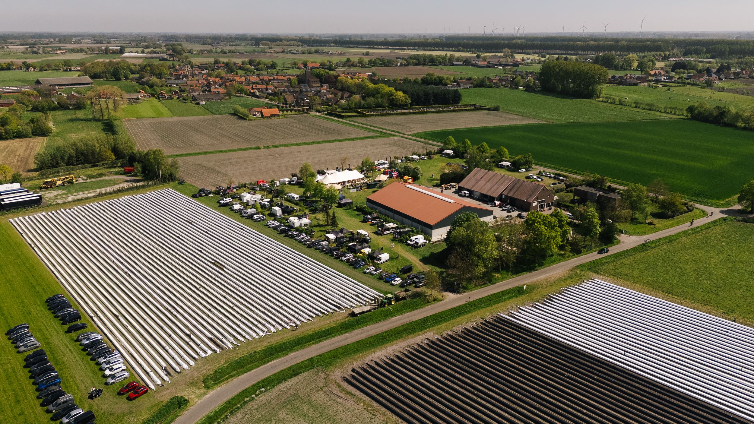 Aerial view of a Dutch farm surrounded by solar panels and greenhouse rows amid lush green agricultural fields.