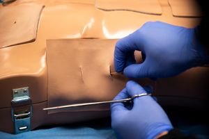 Closeup image of gloved hands making surgical incision in a medical manikin dummy to practice inserting tubes.