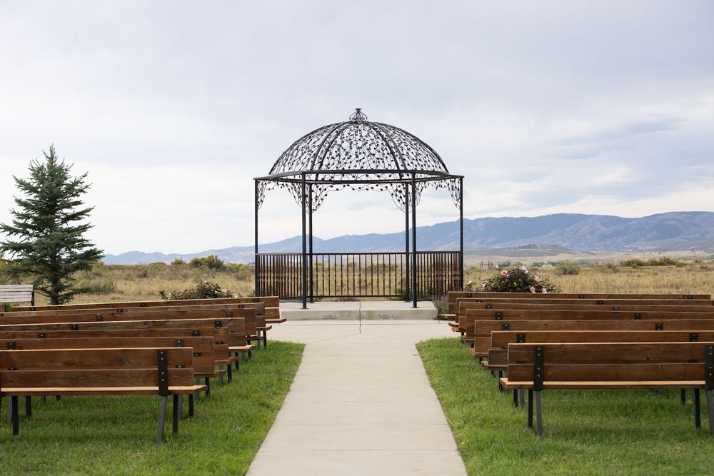 Outdoor wedding ceremony venue with wooden pews, iron gazebo, and scenic mountain views under a cloudy sky.