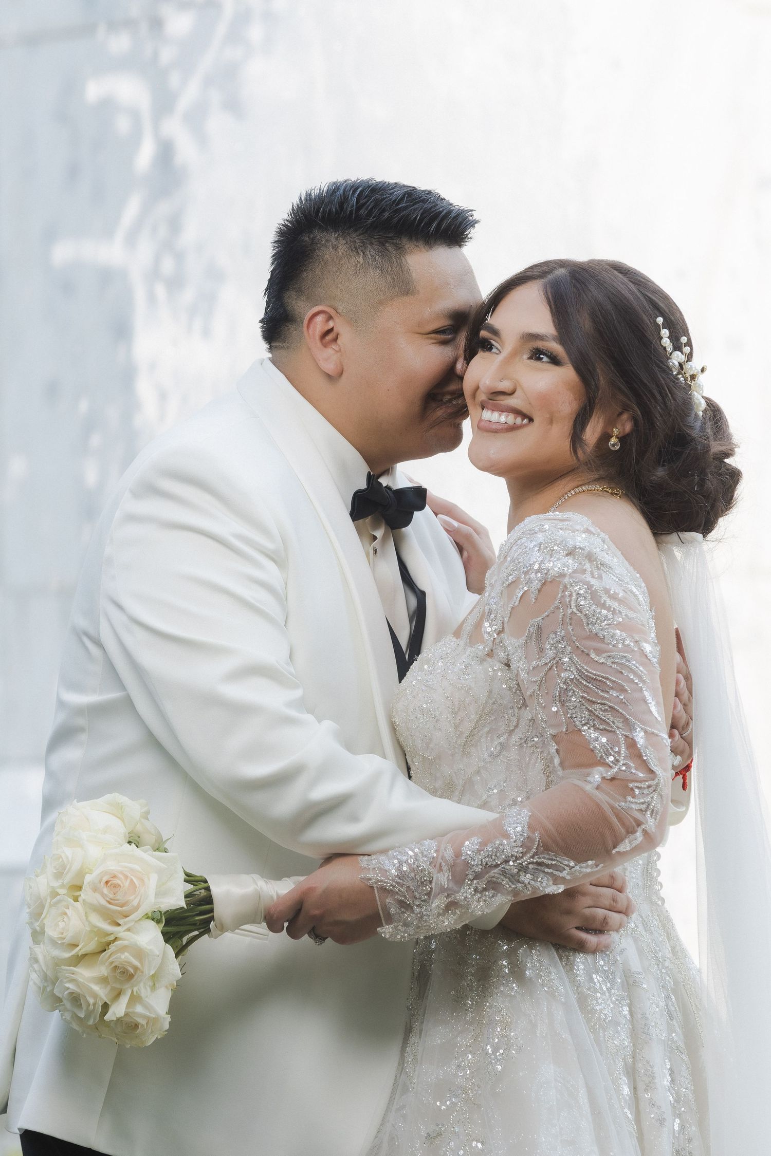 Romantic wedding moment captured against white architectural backdrop.