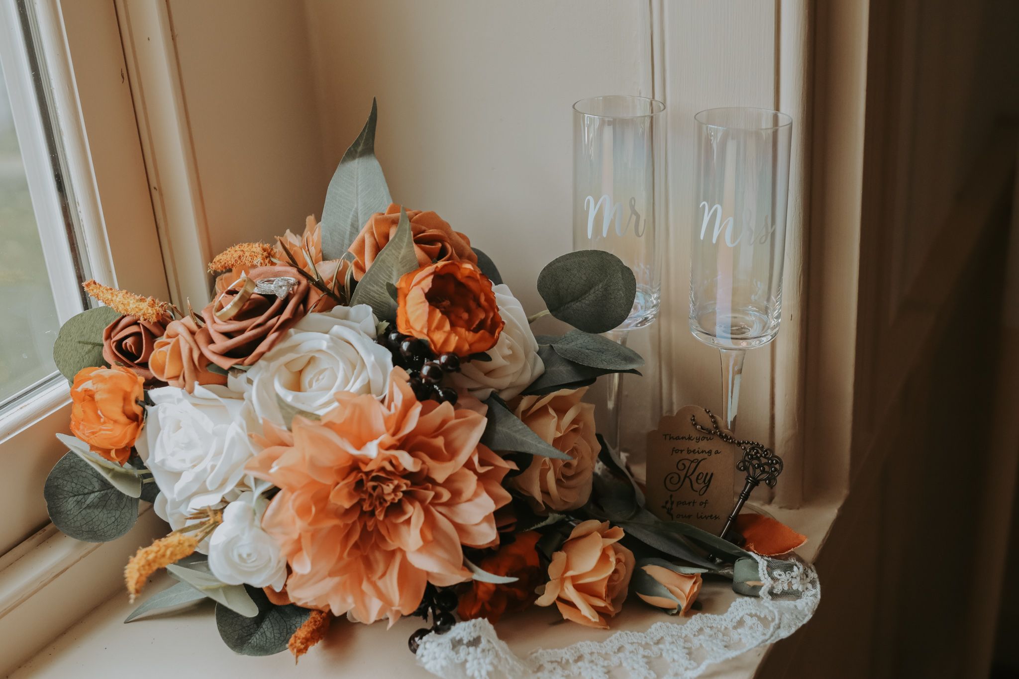 Peach and coral floral arrangement with roses and eucalyptus sits on windowsill.