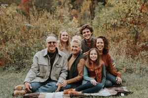 Multi-generational family sits together during autumn outdoor photo session.