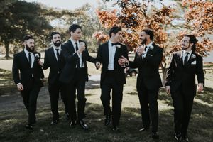 Groomsmen in black suits walking and laughing together outdoors during fall wedding.