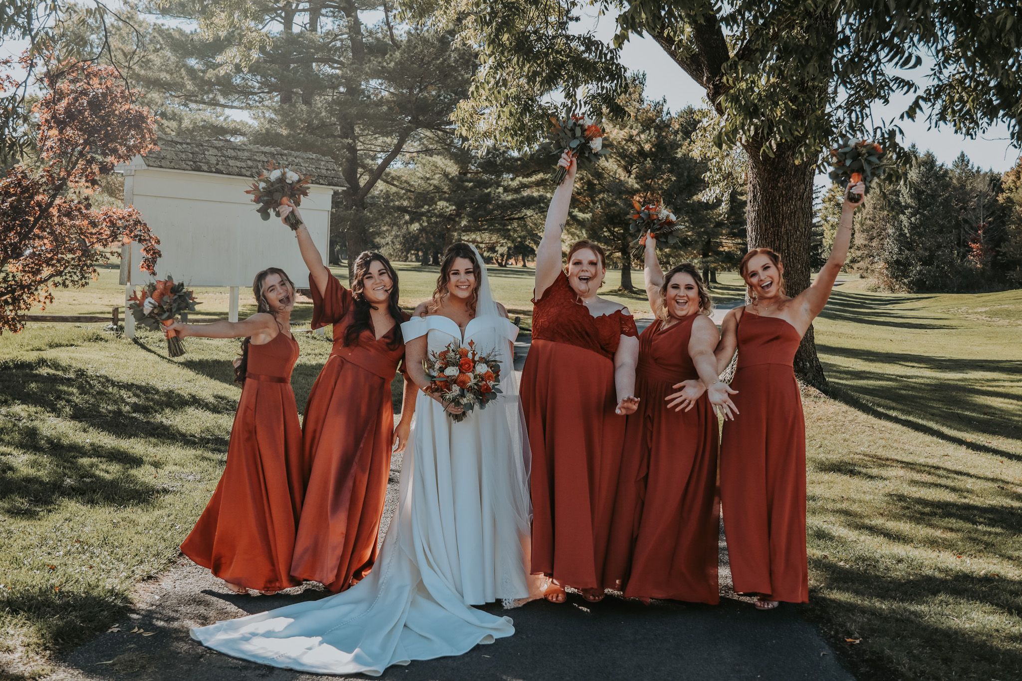 Wedding party with bridesmaids in burgundy dresses and bride pose outdoors.