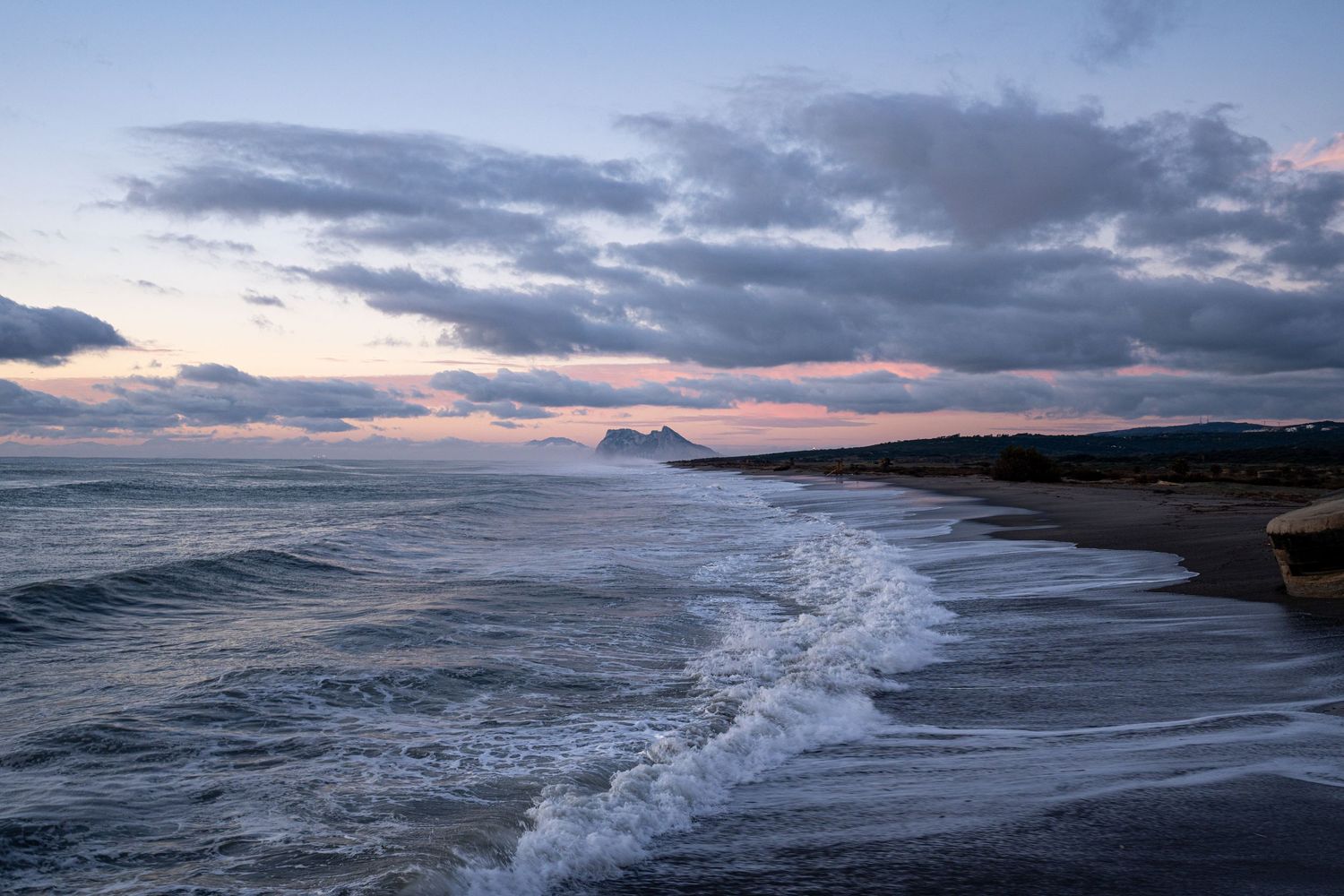 waves onto bunker beach at sunrise gibraltar in distance