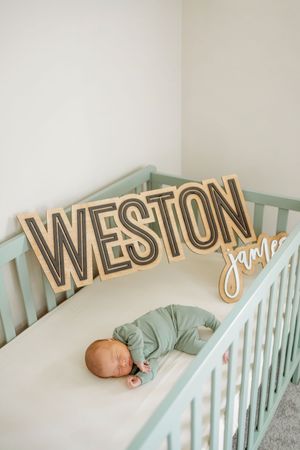 Mint green crib with wooden name letters spelling 'Weston' mounted on white wall.