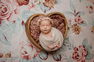 Artistic newborn photography against floral backdrop with vintage styling elements.
