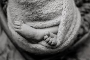 Black and white close-up of newborn wrapped in soft textured fabric.