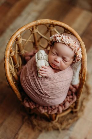 Newborn photography featuring soft pink wrapping in a natural woven basket with rustic elements.