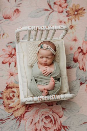 Newborn portrait in white wooden crate against floral backdrop with vintage styling.