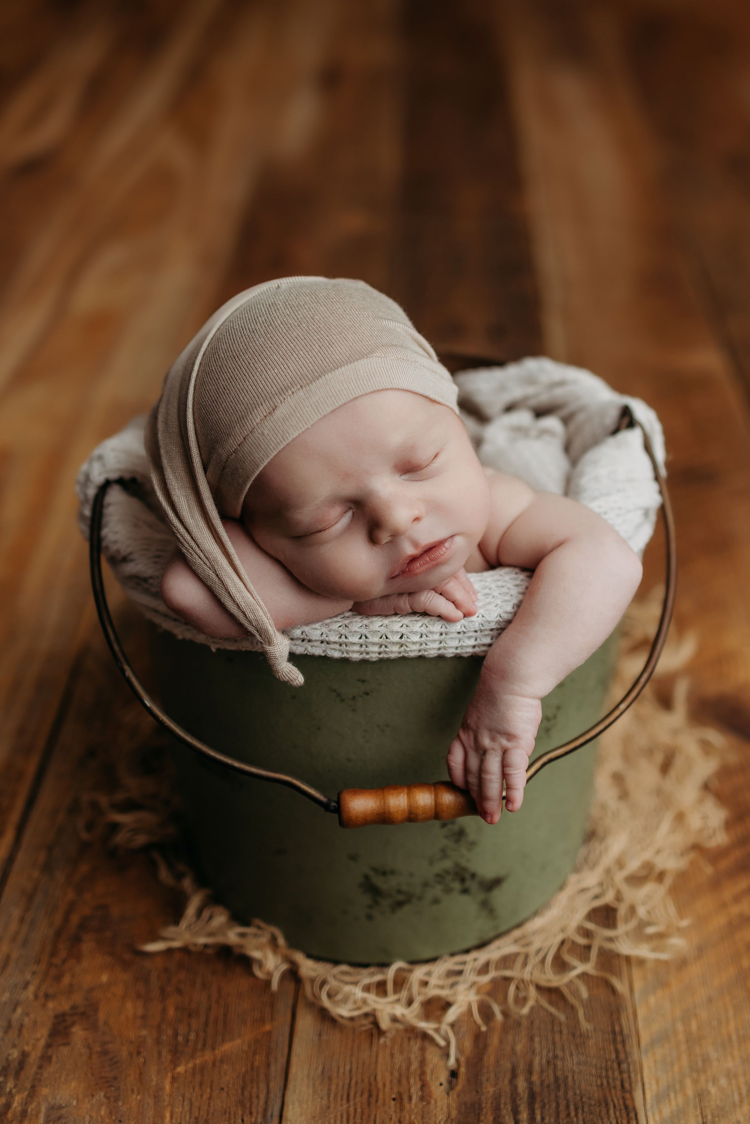 Sleeping newborn nestled in cozy green vintage bucket with knitted blanket on wooden floor.