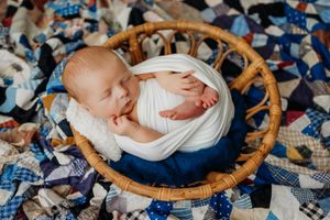 Newborn portrait on blue patterned quilt with woven basket and delicate wrapping.