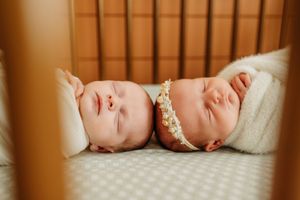 Two sleeping newborn babies lying side by side in a crib wearing floral headbands.