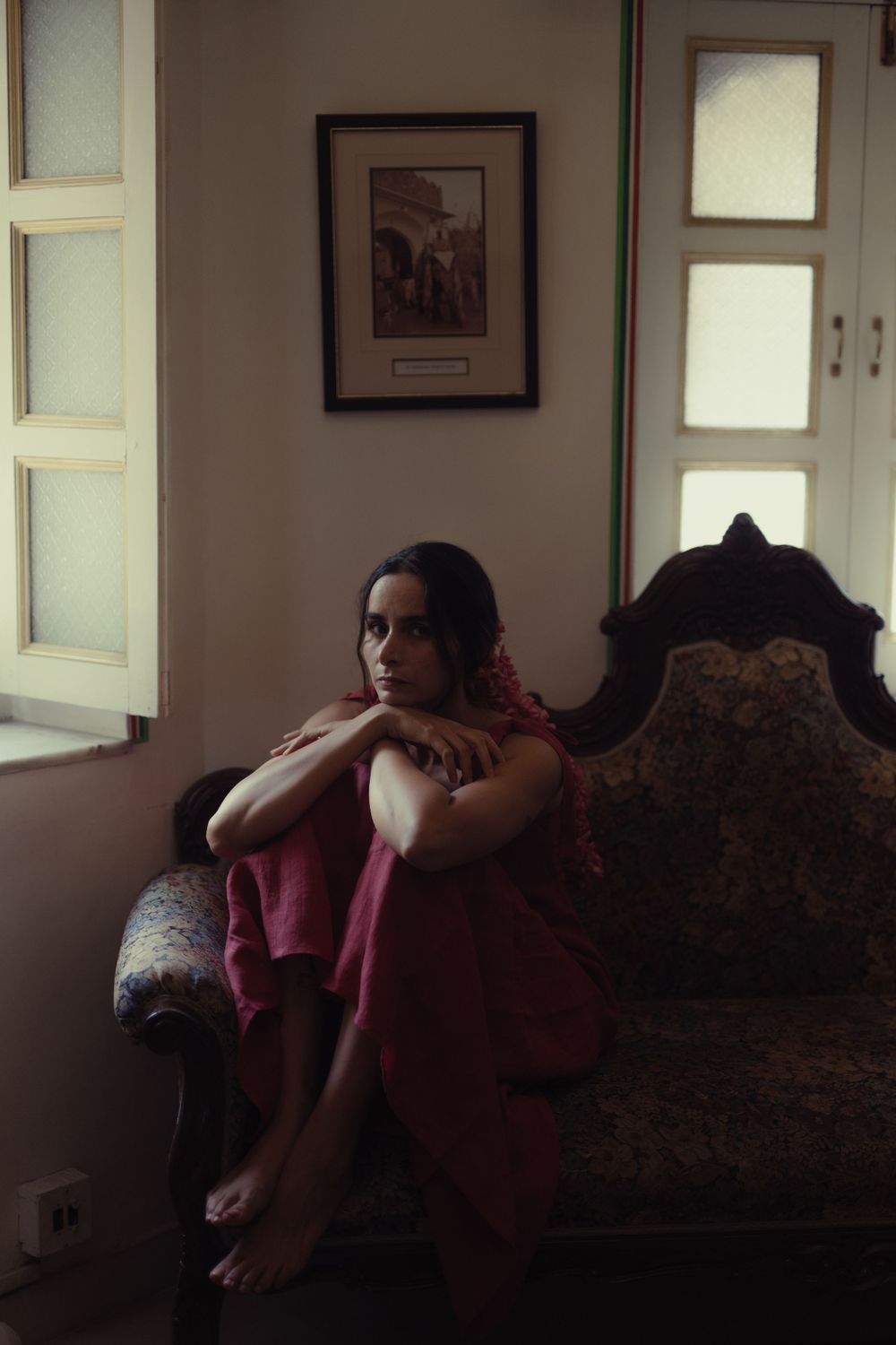 Moody indoor portrait showing someone resting on an antique sofa near a window.