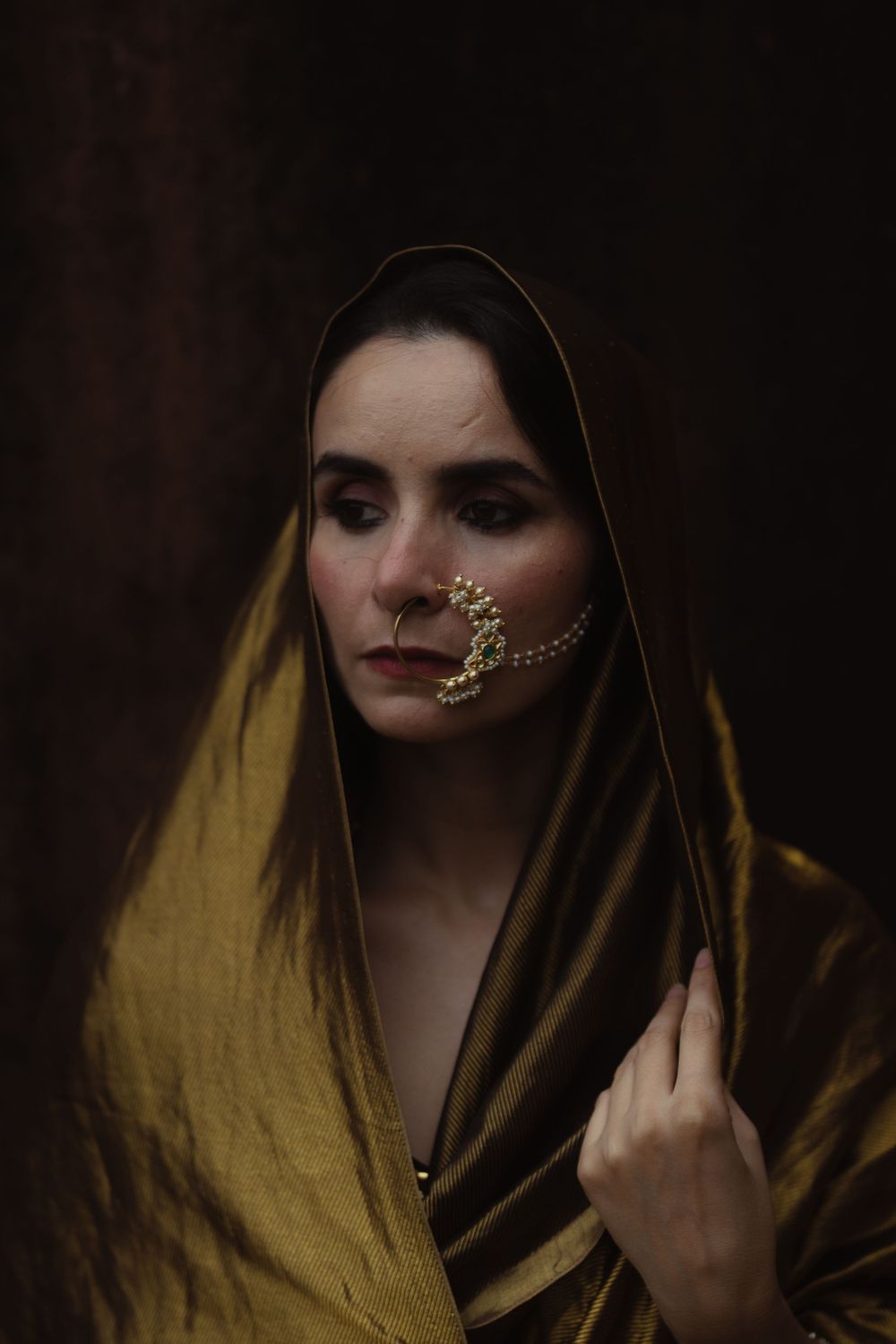 Artistic portrait featuring someone in a mustard yellow draped fabric with decorative face jewelry.