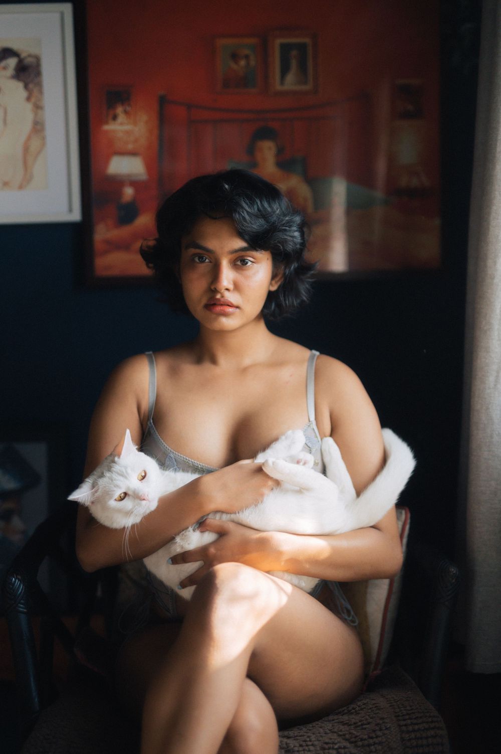 Intimate portrait with white cats in bedroom setting with vintage art posters on red wall.