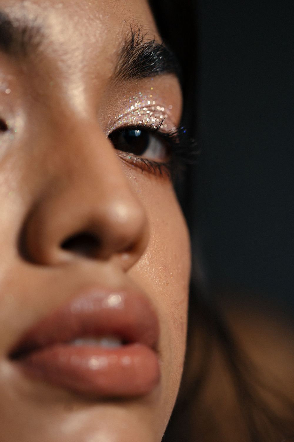 Close-up beauty shot showing glittery eye makeup and glossy lips in warm lighting.