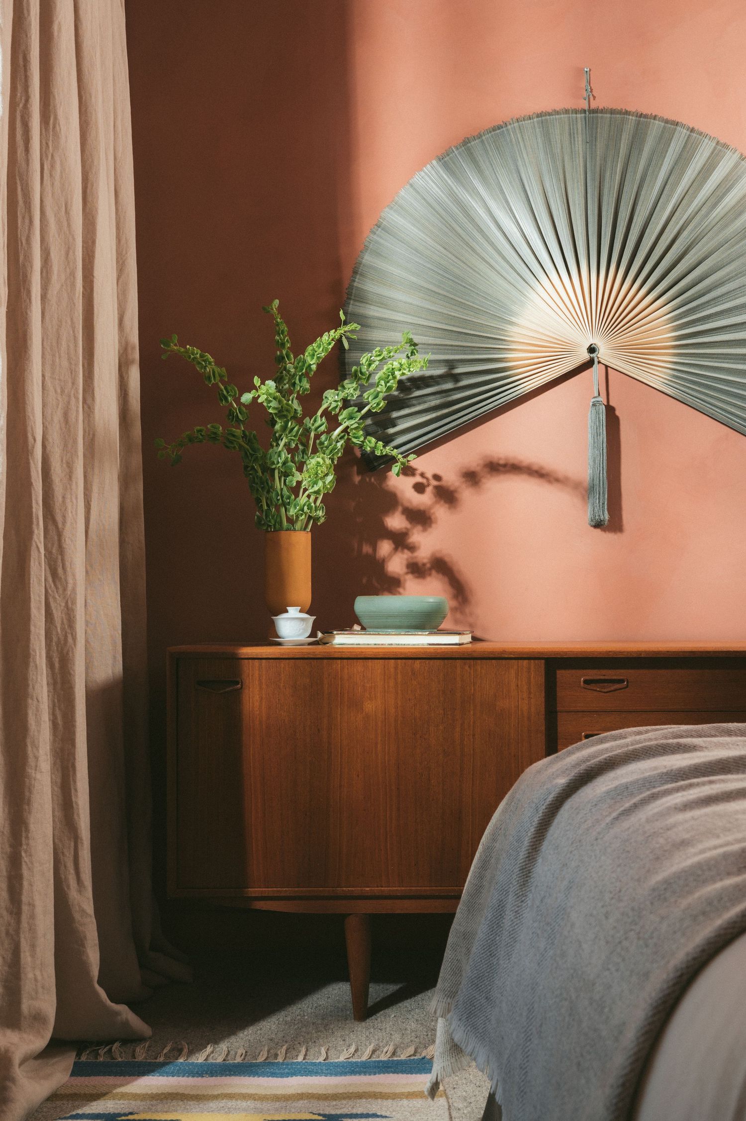 Modern mid-century style room with decorative fan art, wooden furniture, and pink accent wall in warm lighting.