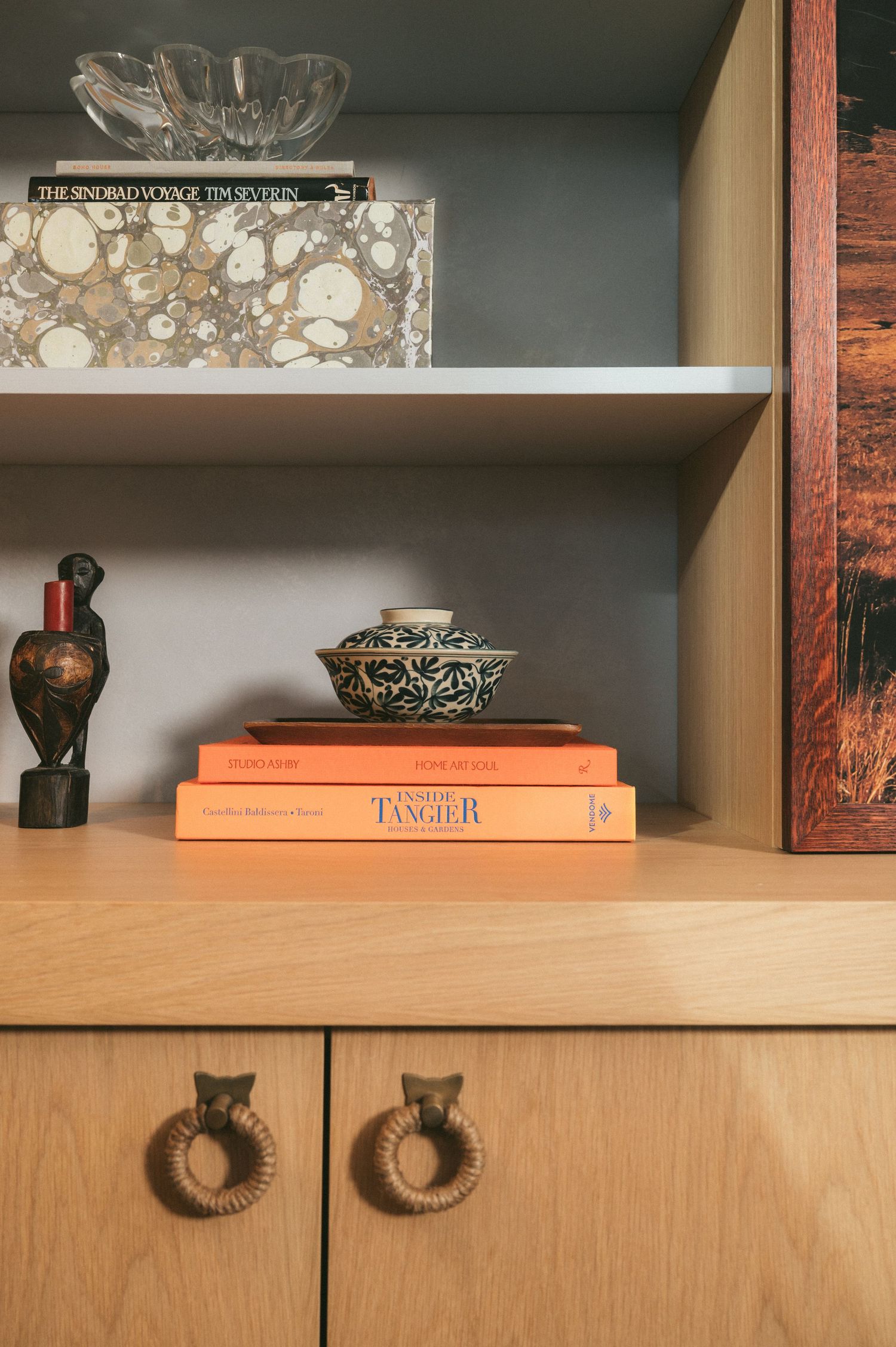 Wooden cabinet shelves displaying decorative objects, books, and vases in warm lighting with orange accents.