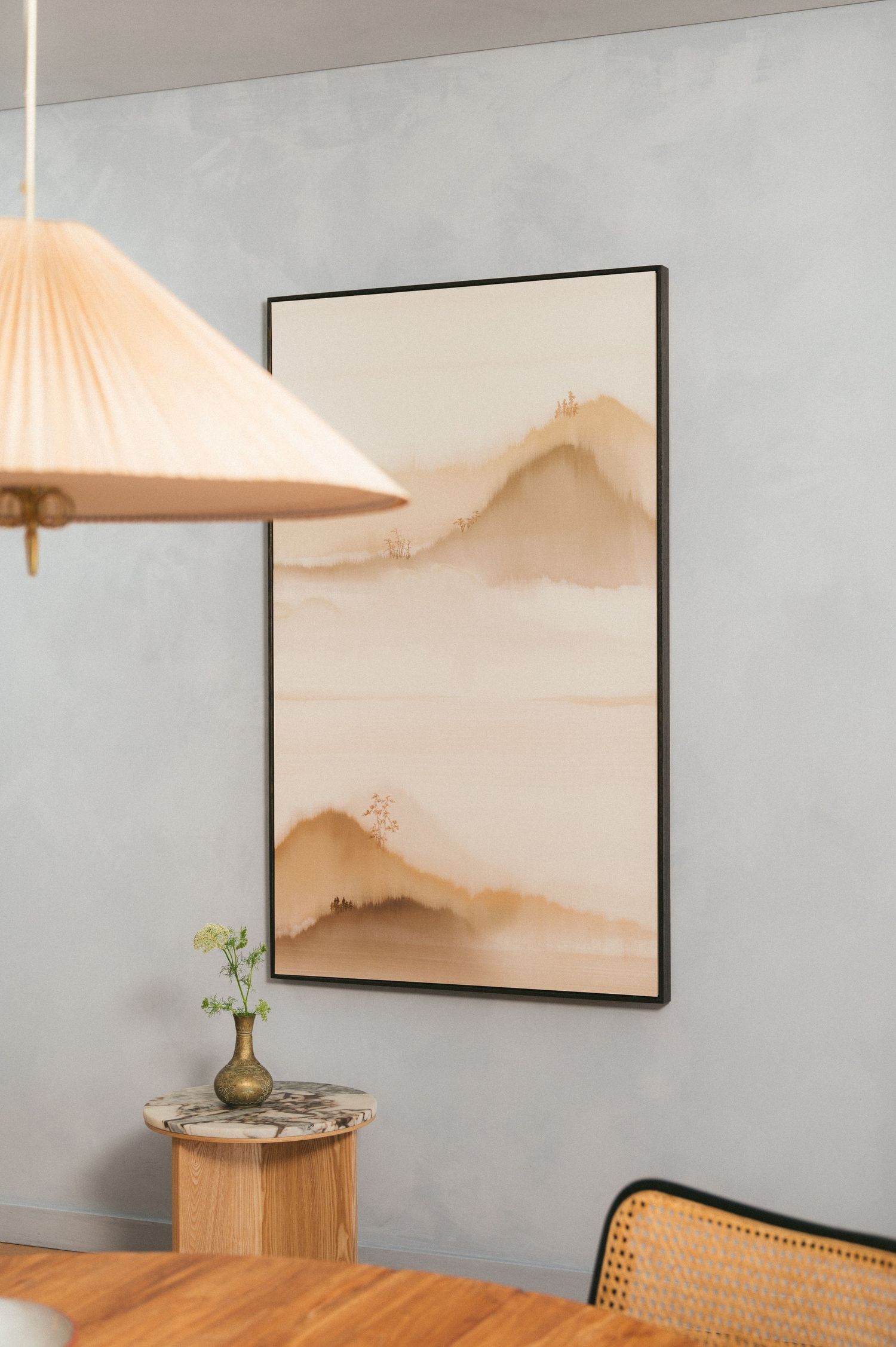 Modern minimalist interior with abstract mountain artwork, pendant lamp, and wooden side table with small vase against gray wall.