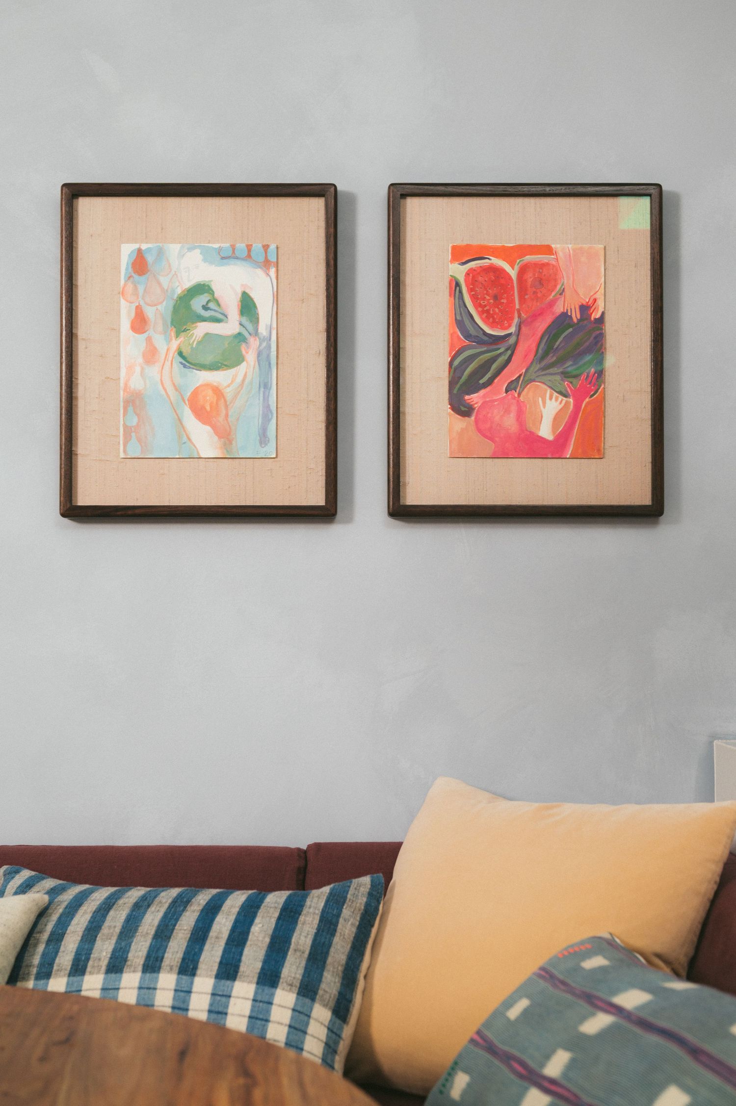 Two framed abstract art pieces with organic shapes in coral and green tones hang above a couch with striped and solid pillows.