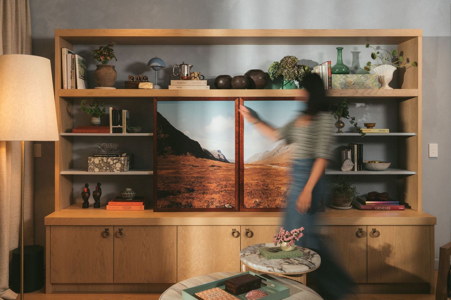 A wide panoramic view of modern apartment shelving with wooden cabinets and decorative plants illuminated by warm lighting.
