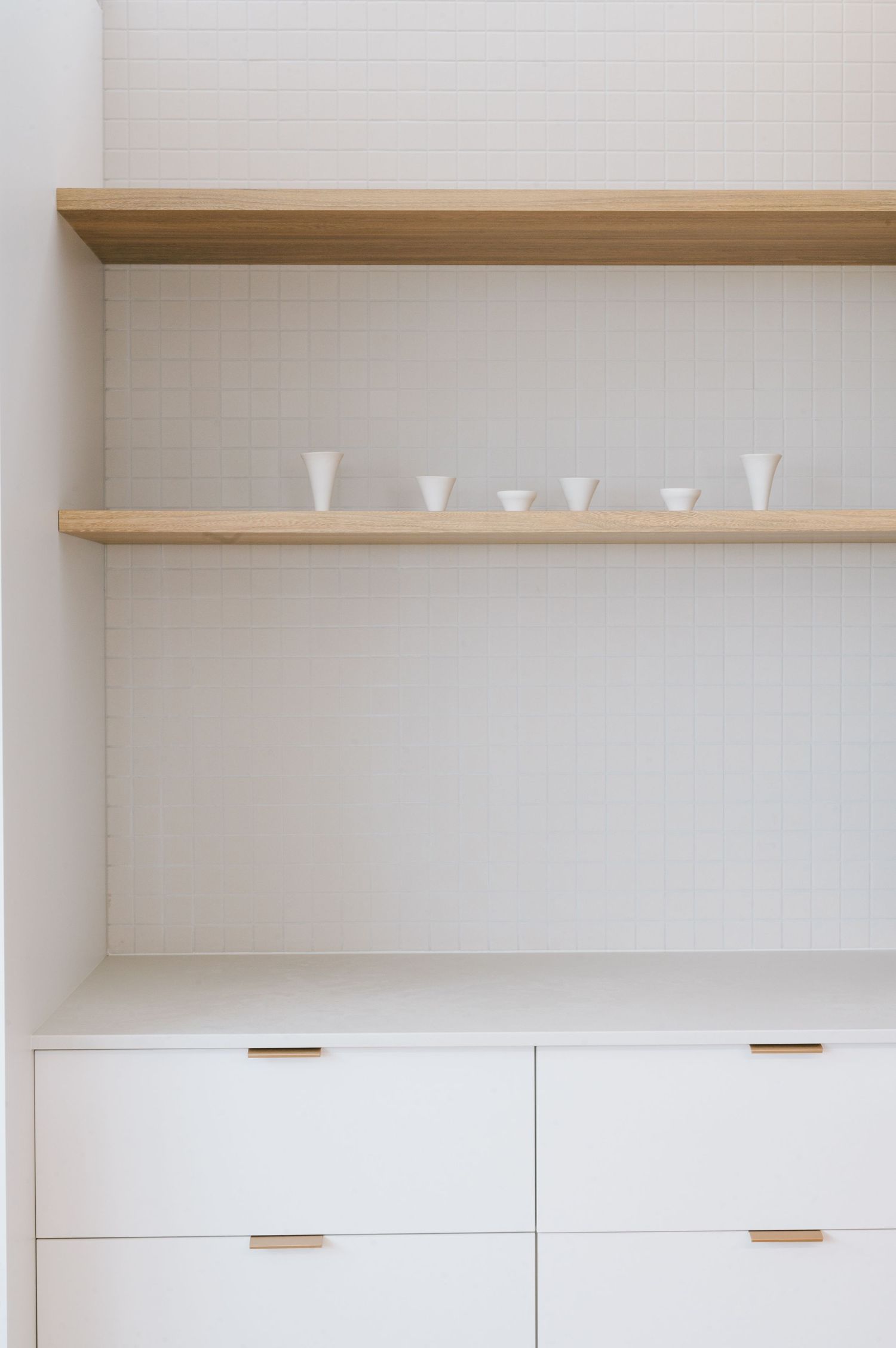 White built-in storage cabinets with wooden shelves displaying minimal white ceramic vessels.