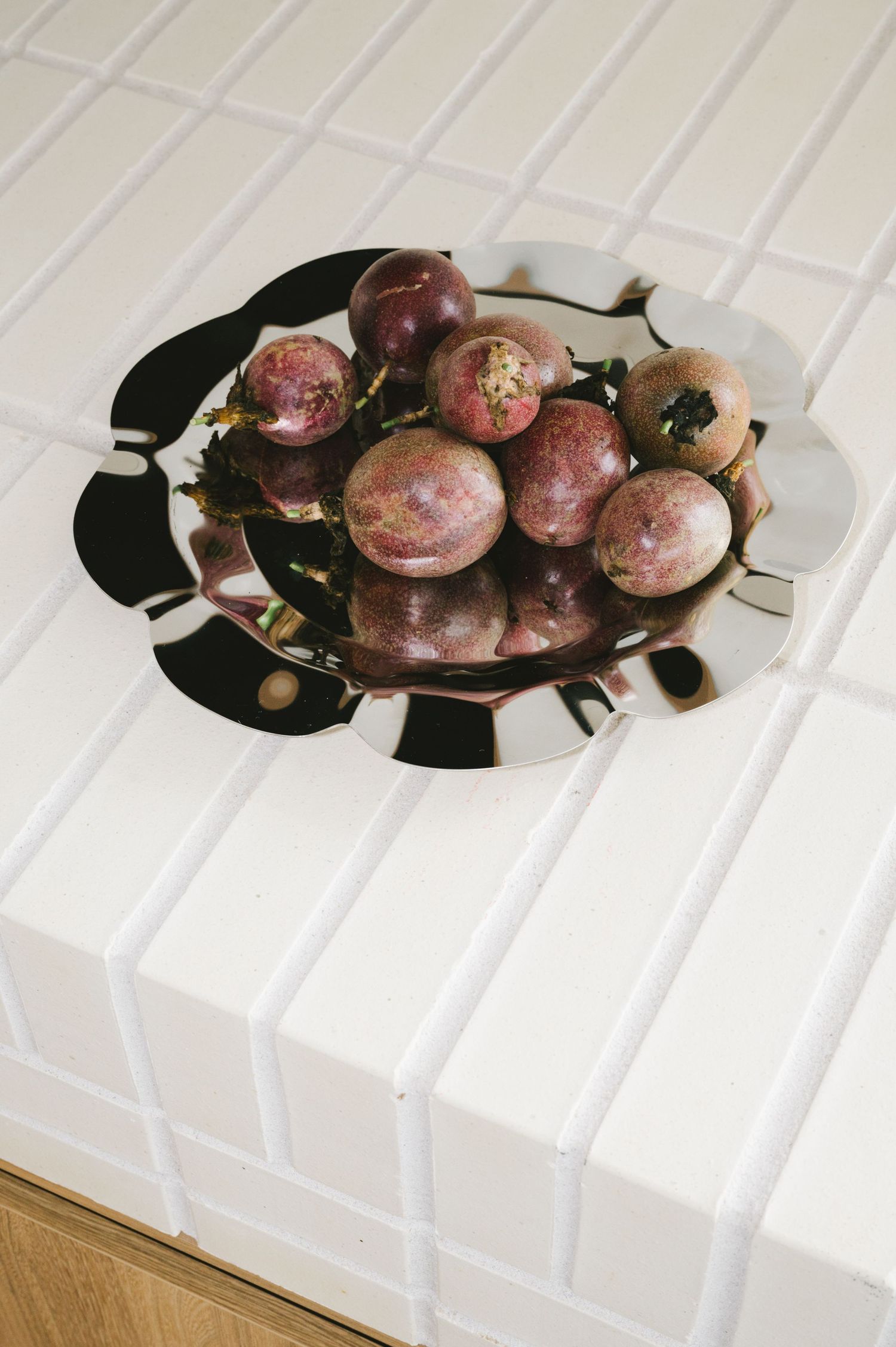 Fresh plums displayed on a decorative black and white plate on a white tiled surface.