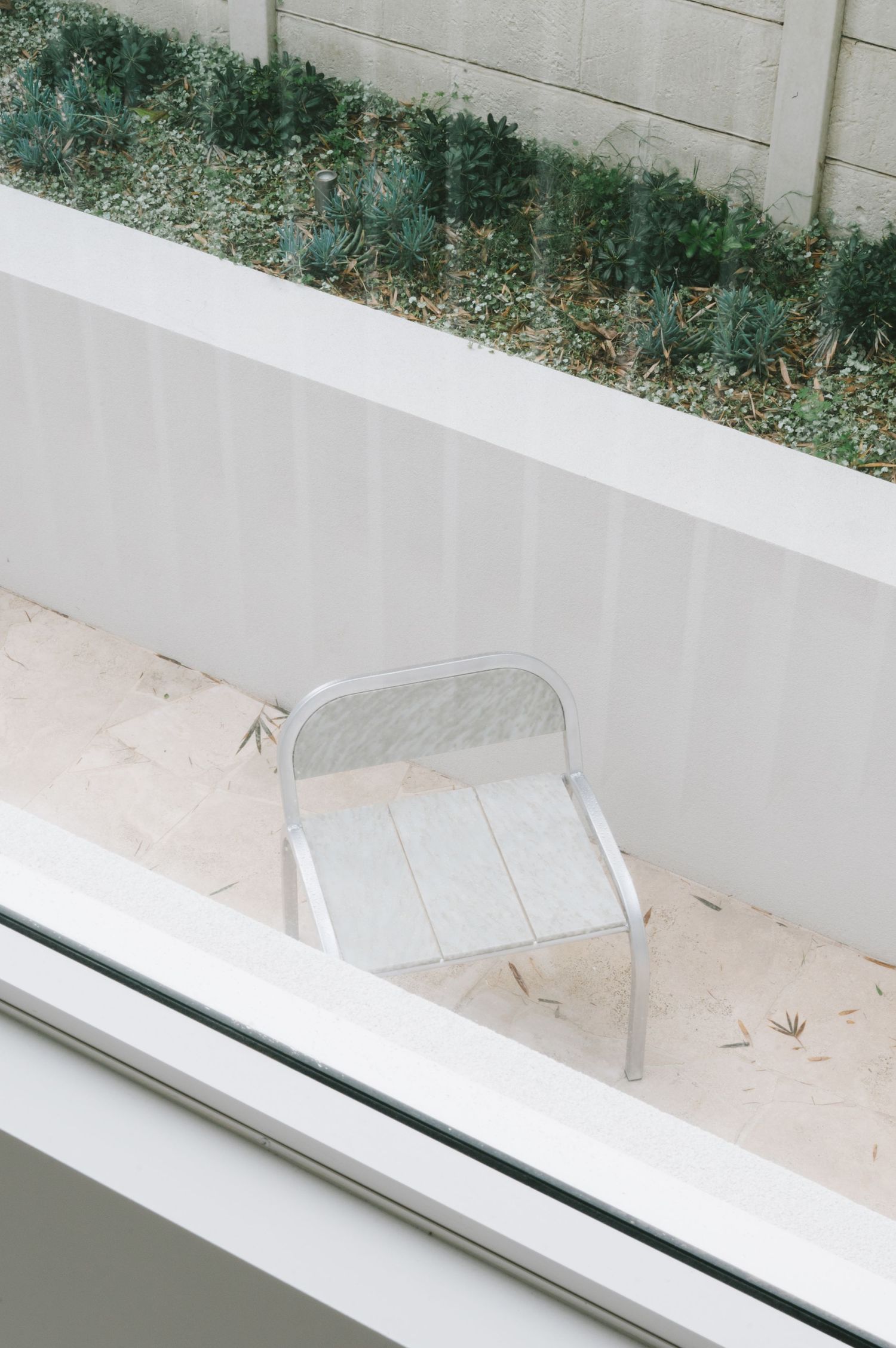 Minimalist outdoor space with metal chair against white wall and greenery.