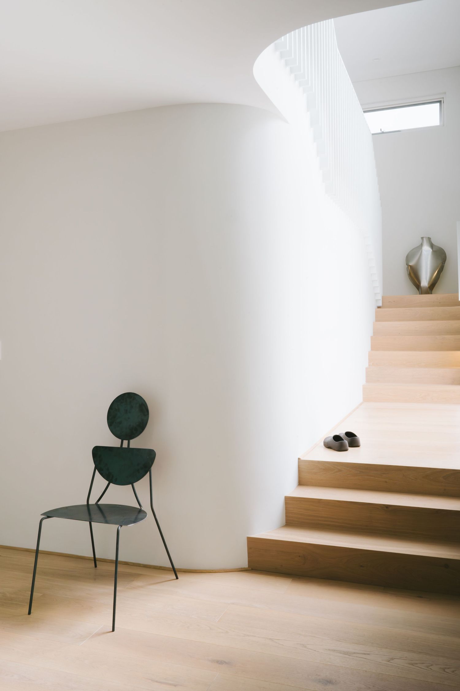 Curved white staircase with wooden steps and minimalist green metal chair at the base.