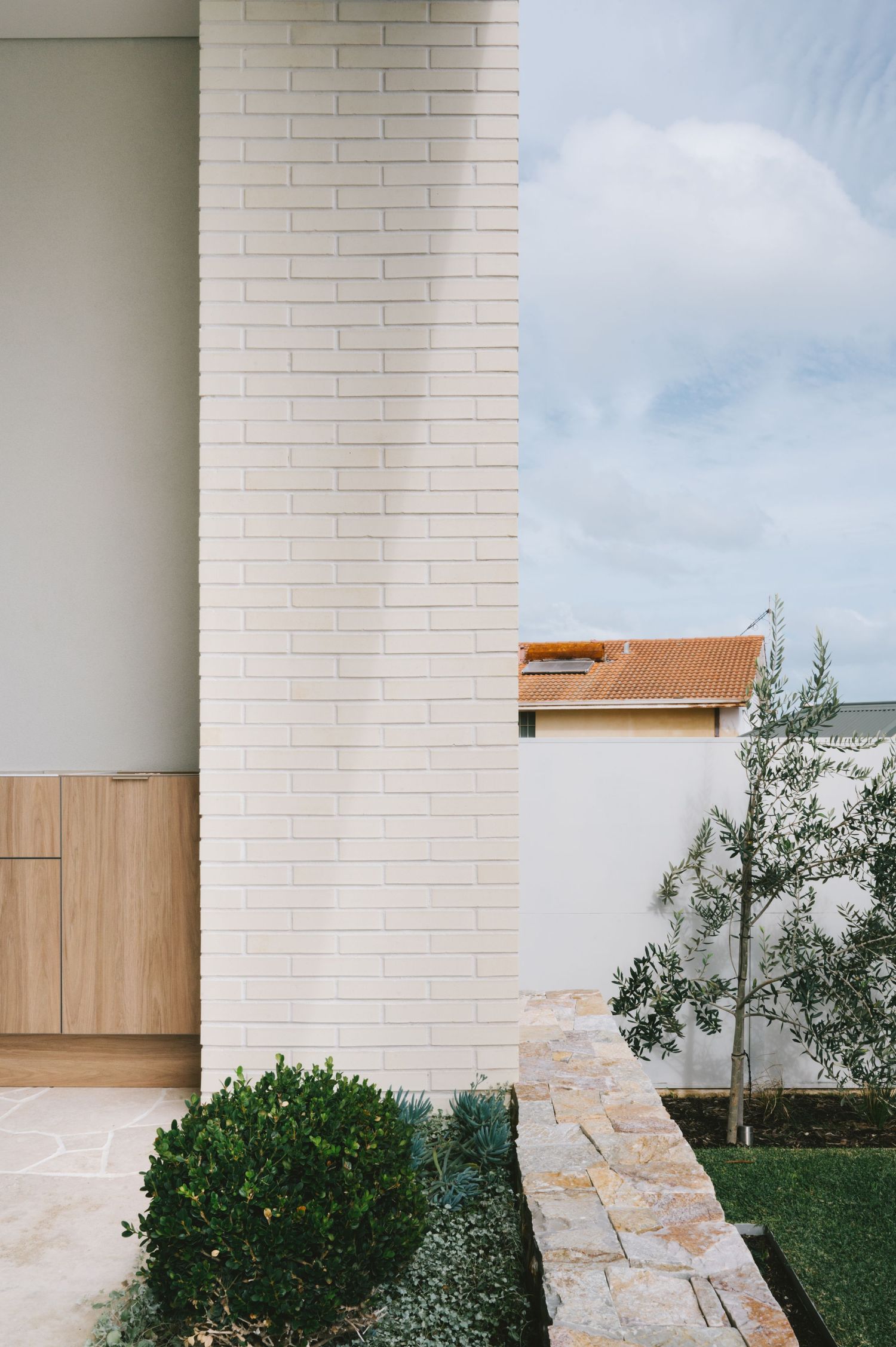 Modern architectural detail showing white brick wall, wooden panels and landscaped garden path.