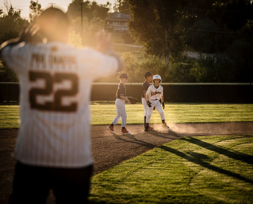 Youth baseball players on a field bathed in warm golden sunset light during a little league game.