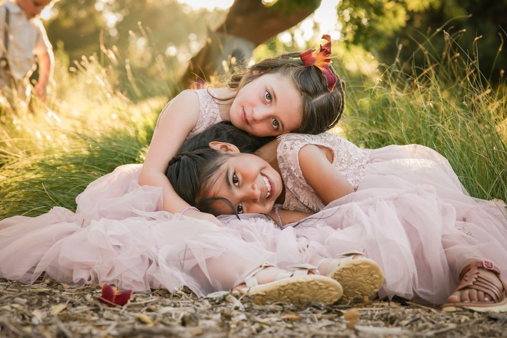 Two young girls in pink tulle dresses lying together on the ground outdoors in golden sunlight. Ramona CA photographed by solstice&willow